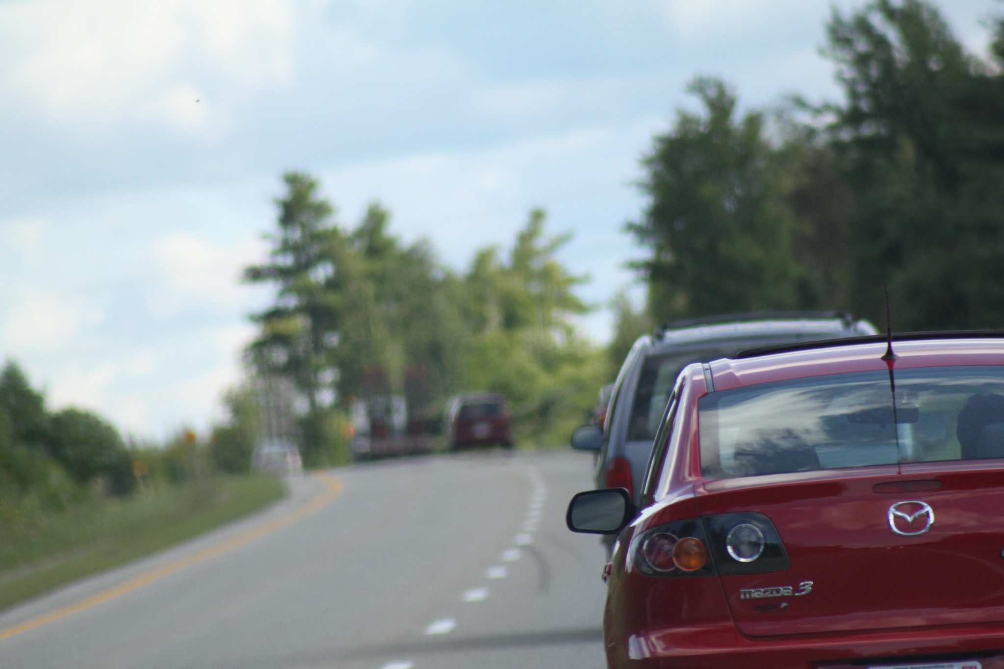 Mazda 3 движется в транспортном потоке по двухполосной лесной дороге вне населенного пункта